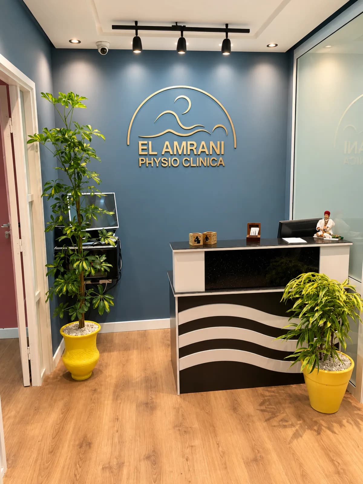Accueil d’El Amrani Physio Clinica avec comptoir à vagues, enseigne dorée et plantes vertes