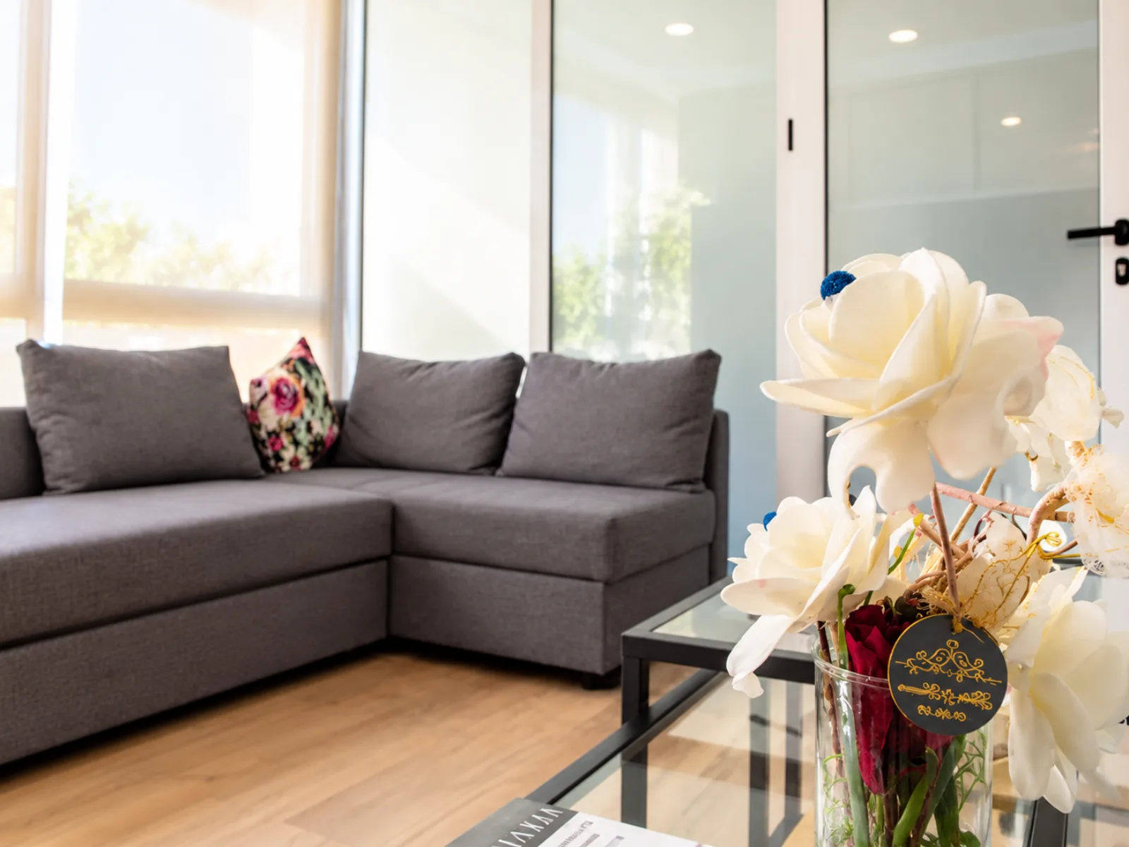 Espace d’attente lumineux avec canapé gris, table basse en verre et fleurs