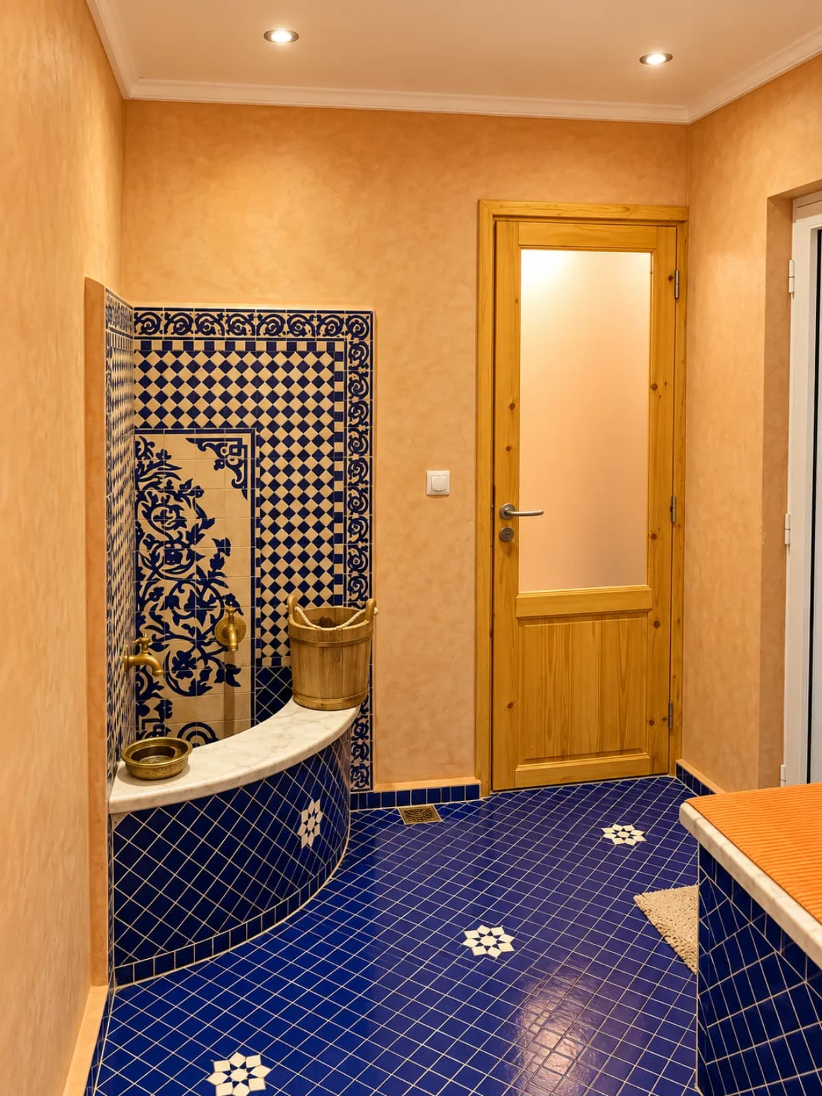 Hammam traditionnel avec zellige bleu, banquette en marbre, robinets en laiton et seau en bois